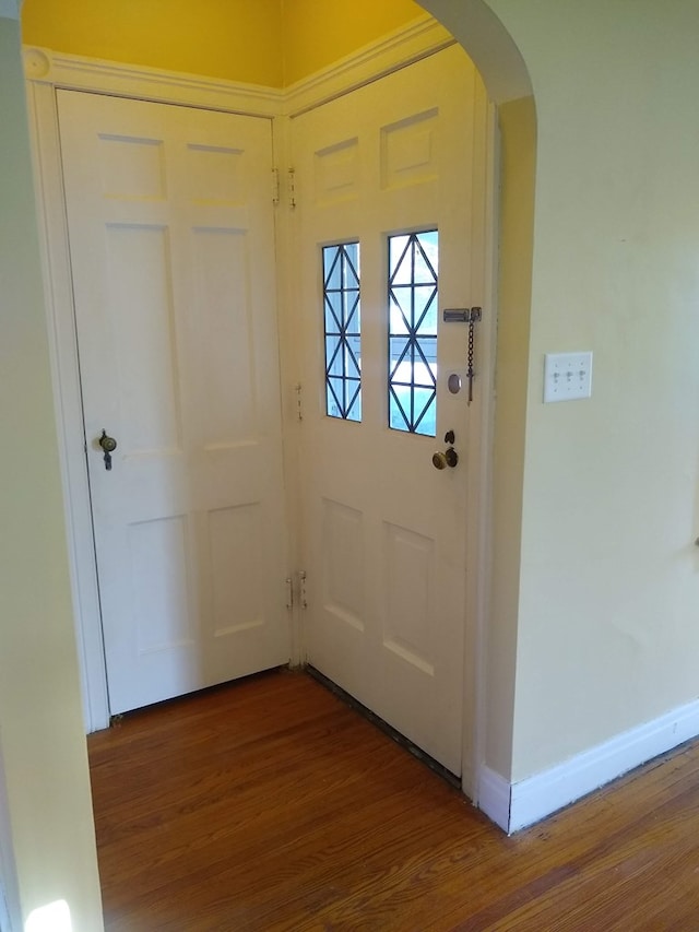 doorway to outside with wood finished floors, baseboards, and arched walkways