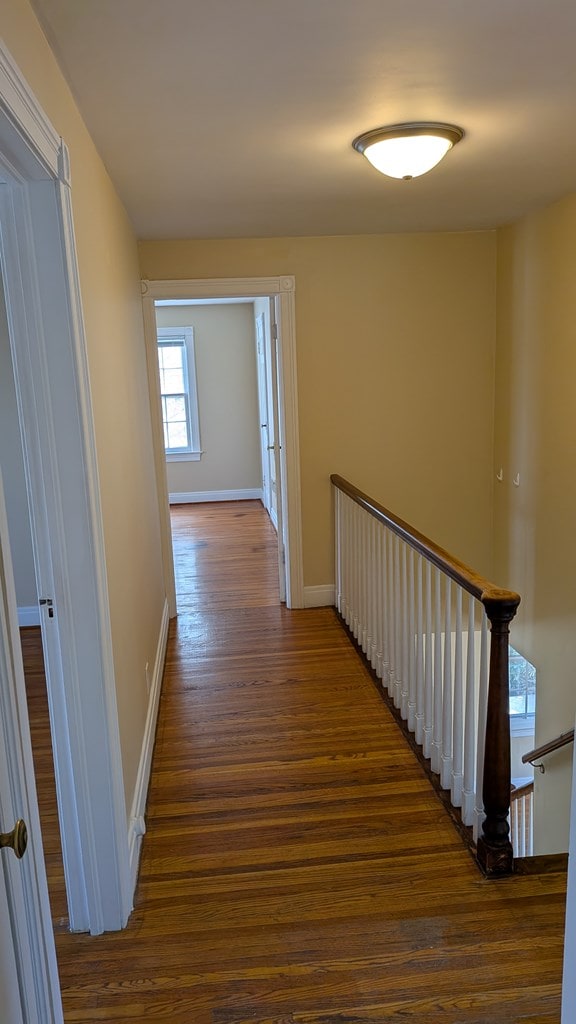 hall featuring an upstairs landing, dark wood-type flooring, and baseboards