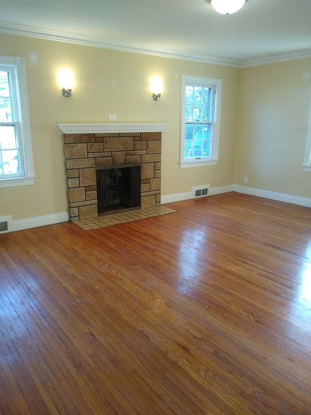 unfurnished living room featuring visible vents, ornamental molding, a fireplace, a wealth of natural light, and wood finished floors
