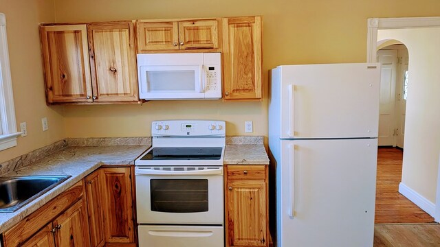 kitchen with a sink, white appliances, light wood-type flooring, light countertops, and arched walkways