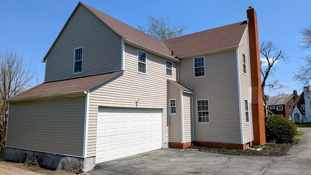rear view of house with a chimney, driveway, and an attached garage