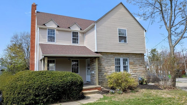 view of front facade featuring roof with shingles, a chimney, covered porch, and stone siding