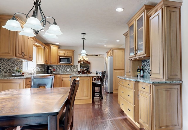 kitchen with a center island, hanging light fixtures, dark hardwood / wood-style flooring, stainless steel appliances, and light stone countertops