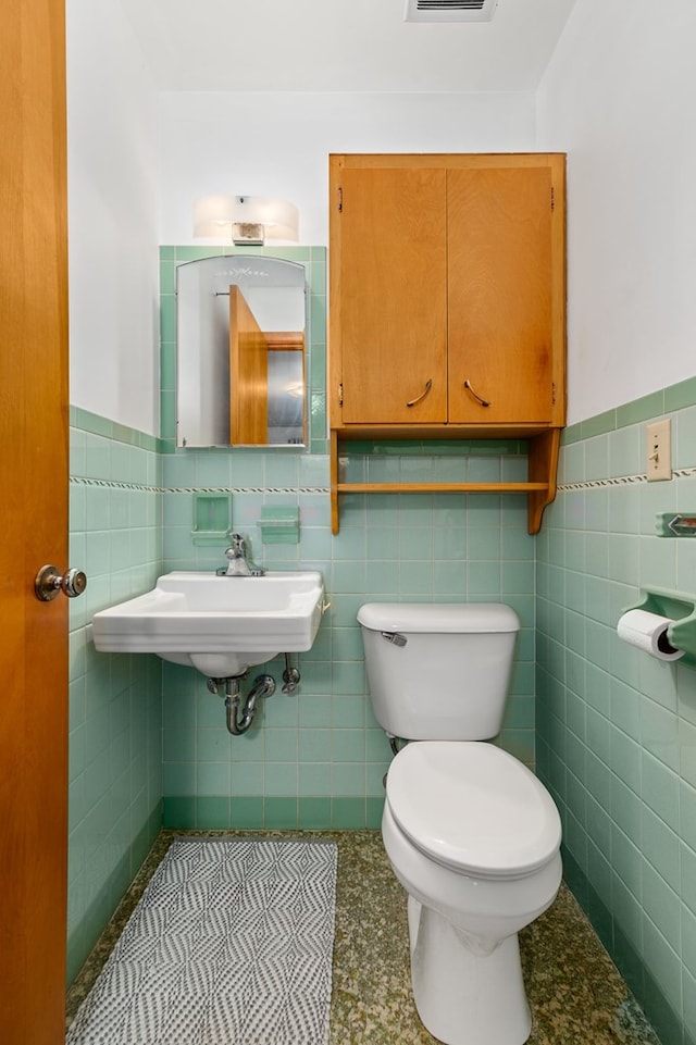 bathroom featuring toilet, tile walls, and sink