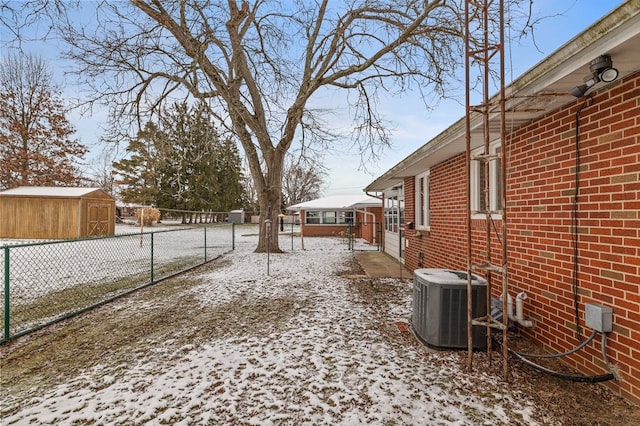 yard covered in snow with central AC unit and a storage shed