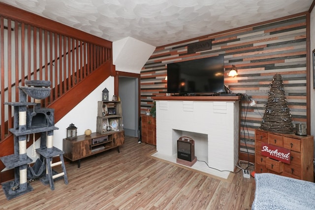 living room featuring a textured ceiling, a fireplace, wood finished floors, wallpapered walls, and stairway