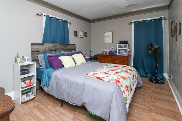 bedroom featuring ornamental molding, light wood-style floors, and visible vents