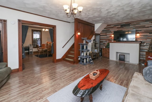 living room featuring crown molding, stairs, a fireplace, wood finished floors, and a notable chandelier