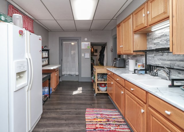 kitchen featuring a sink, white refrigerator with ice dispenser, decorative backsplash, dark wood-type flooring, and a drop ceiling