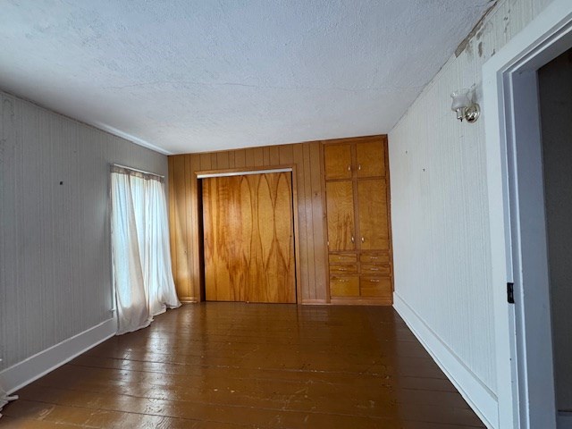 3649 Nazor Rd, Crestline, OH 44827 - unfurnished bedroom with wood-type flooring, wooden walls, a closet, a textured ceiling, and baseboards
