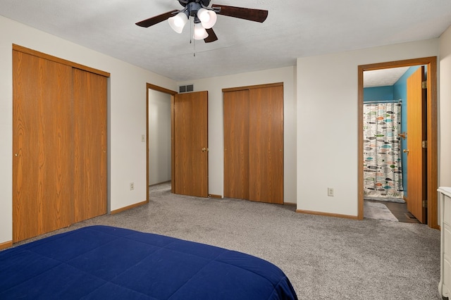 unfurnished bedroom featuring ceiling fan, light colored carpet, ensuite bathroom, and multiple closets