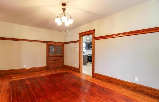 spare room featuring hardwood / wood-style floors, an inviting chandelier, and baseboards