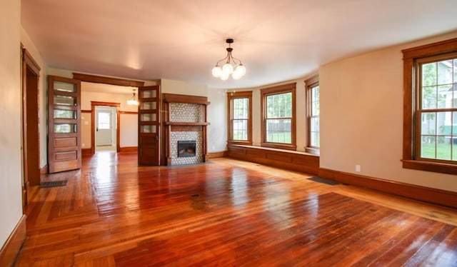 unfurnished living room featuring baseboards, a notable chandelier, hardwood / wood-style floors, and a fireplace