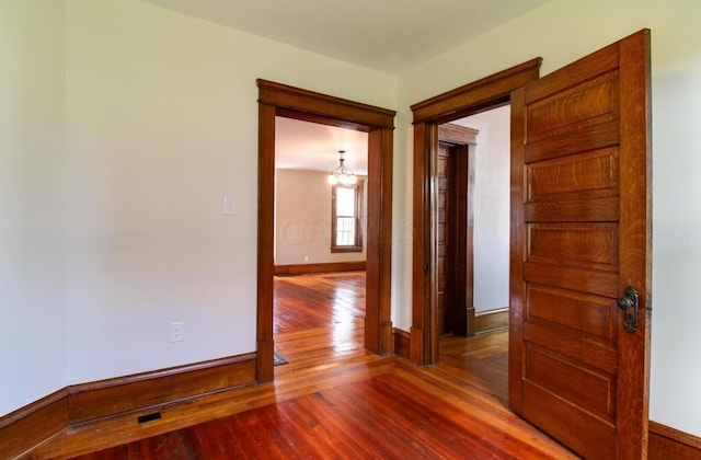 unfurnished room featuring an inviting chandelier, baseboards, and wood-type flooring