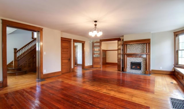 unfurnished living room featuring visible vents, a tiled fireplace, wood finished floors, stairway, and an inviting chandelier