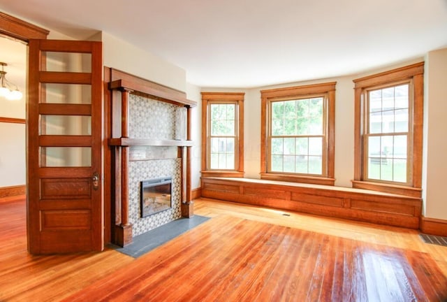 unfurnished living room featuring visible vents, baseboards, wood finished floors, and a tile fireplace