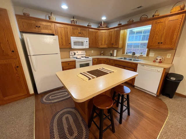 kitchen featuring a kitchen bar, white appliances, sink, light hardwood / wood-style flooring, and a center island