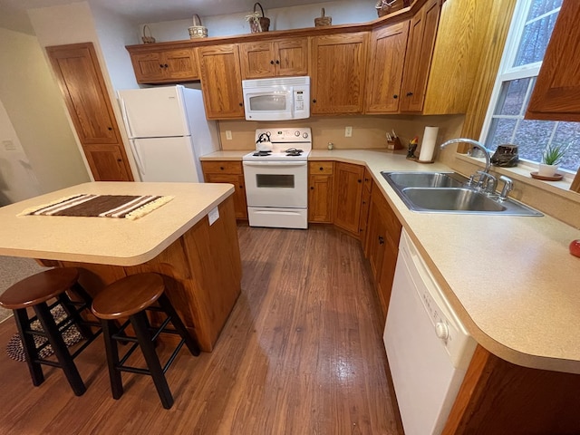 kitchen with white appliances, dark hardwood / wood-style floors, a breakfast bar area, and sink