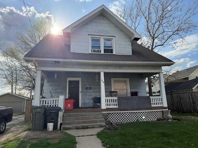 bungalow with fence, covered porch, a front yard, roof with shingles, and an outbuilding