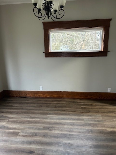 empty room featuring plenty of natural light, baseboards, an inviting chandelier, and wood finished floors