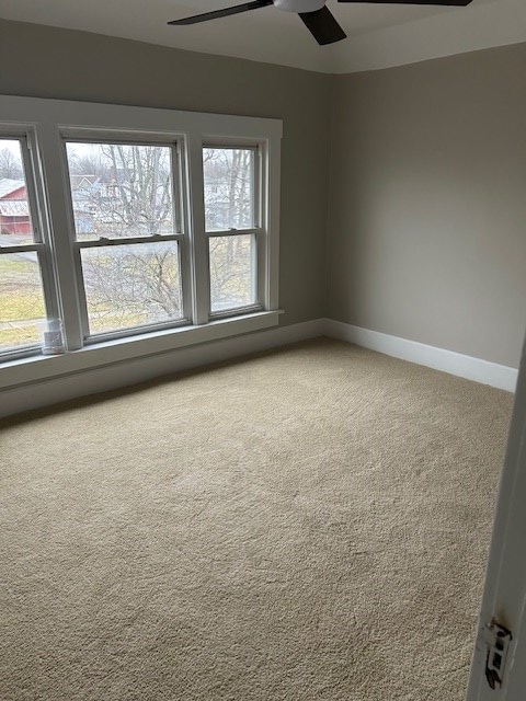 carpeted spare room featuring ceiling fan and baseboards