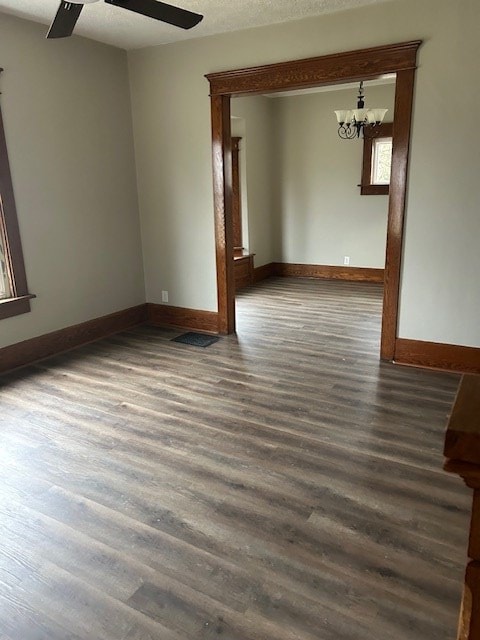 empty room featuring dark wood-style flooring, ceiling fan with notable chandelier, baseboards, and a textured ceiling