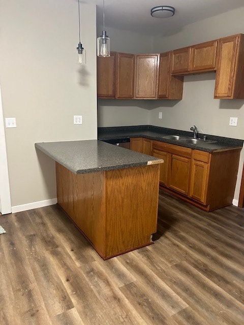 kitchen with a peninsula, brown cabinets, a sink, and dark countertops