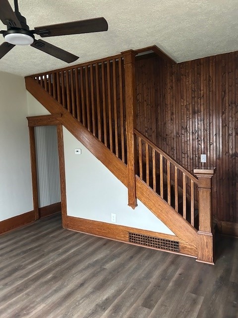unfurnished living room featuring a ceiling fan, a textured ceiling, stairway, wood finished floors, and wood walls