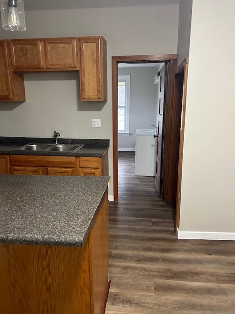 kitchen featuring brown cabinetry, a sink, dark wood-style floors, and baseboards