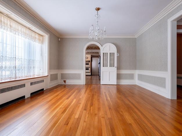 unfurnished dining area featuring crown molding, radiator heating unit, an inviting chandelier, and light hardwood / wood-style flooring