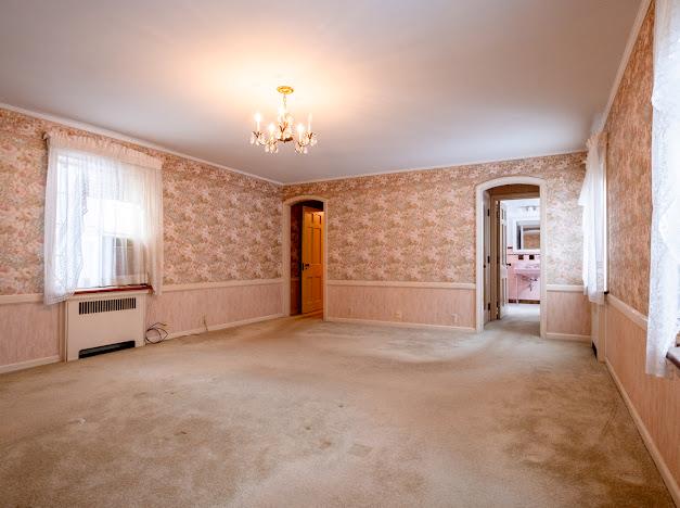 carpeted empty room with radiator heating unit, crown molding, and an inviting chandelier