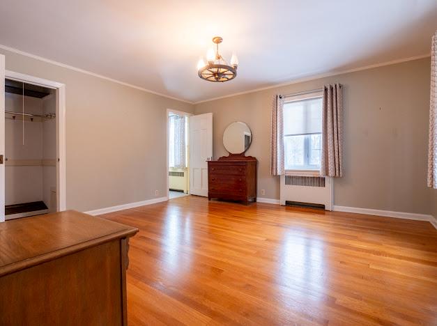 empty room featuring light wood-type flooring, radiator heating unit, ornamental molding, and an inviting chandelier