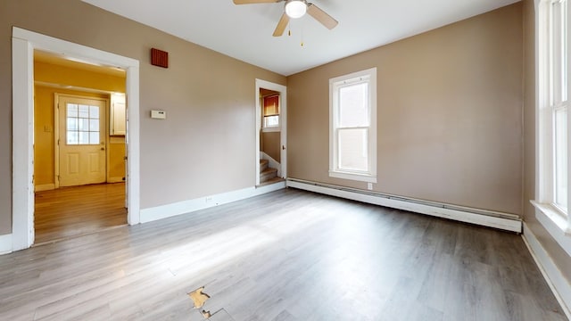 spare room with ceiling fan, light wood-type flooring, and a baseboard heating unit