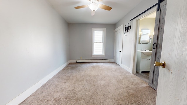 carpeted empty room featuring sink, a barn door, ceiling fan, and baseboard heating