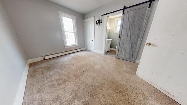 unfurnished bedroom featuring a barn door, a baseboard heating unit, light colored carpet, and ensuite bath