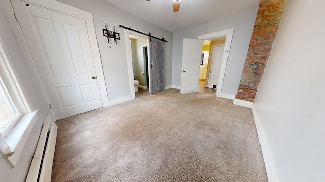 unfurnished bedroom featuring baseboard heating, light colored carpet, a barn door, and ensuite bath