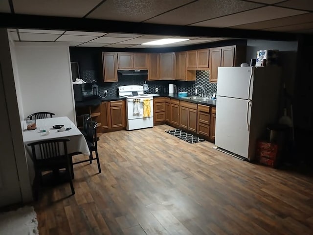kitchen featuring a paneled ceiling, white appliances, sink, decorative backsplash, and wood-type flooring
