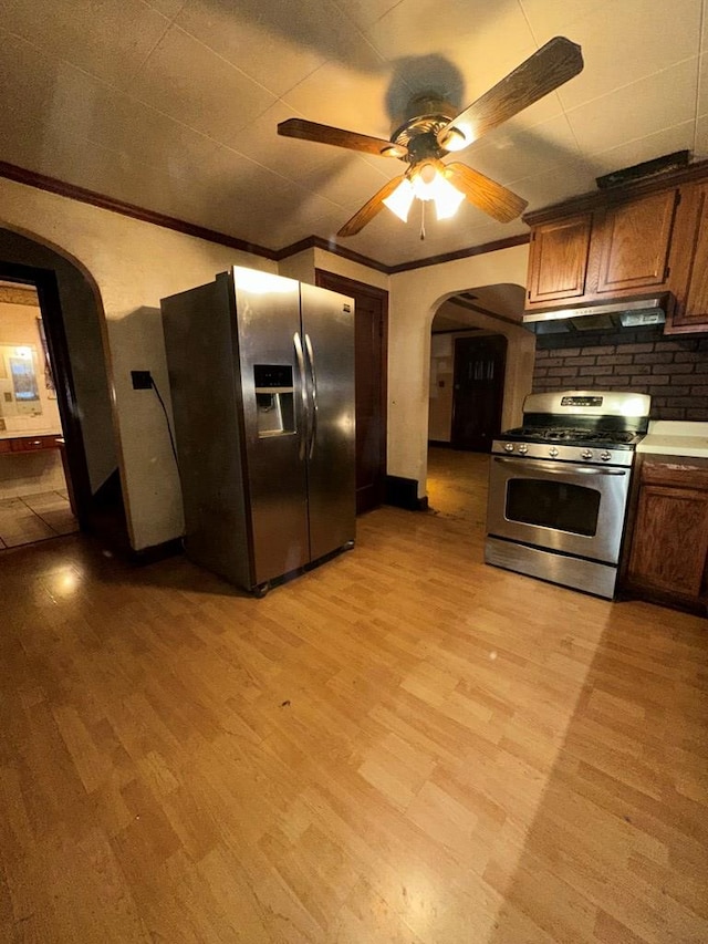 kitchen featuring under cabinet range hood, ornamental molding, light wood-style flooring, appliances with stainless steel finishes, and arched walkways