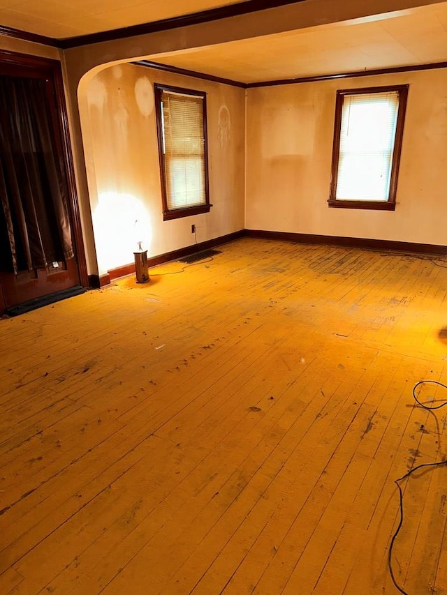 spare room featuring baseboards, arched walkways, crown molding, and hardwood / wood-style flooring