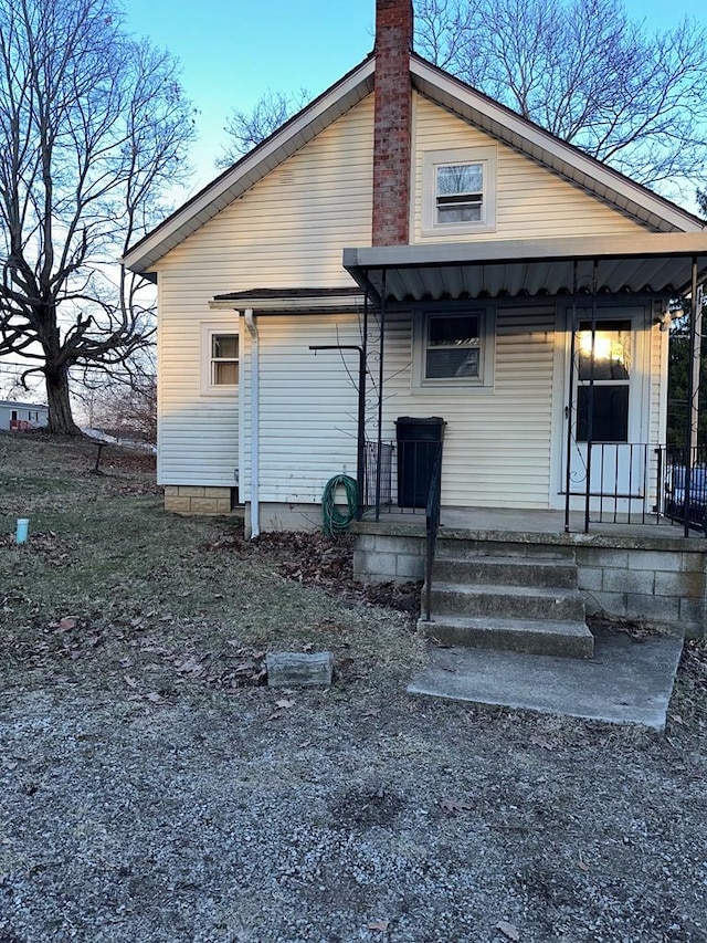 back of property with covered porch and a chimney