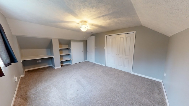 unfurnished bedroom with carpet flooring, a textured ceiling, ceiling fan, a closet, and lofted ceiling