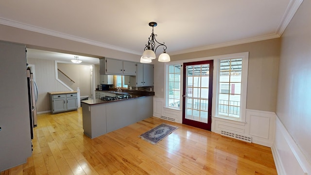 kitchen featuring light wood-type flooring, kitchen peninsula, hanging light fixtures, and ornamental molding