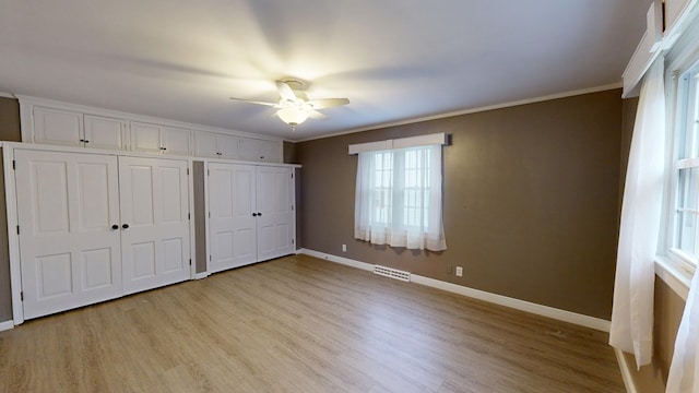 unfurnished bedroom with light wood-type flooring, multiple closets, ceiling fan, and ornamental molding