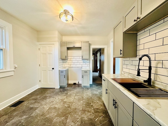 kitchen with gray cabinetry, decorative backsplash, and sink