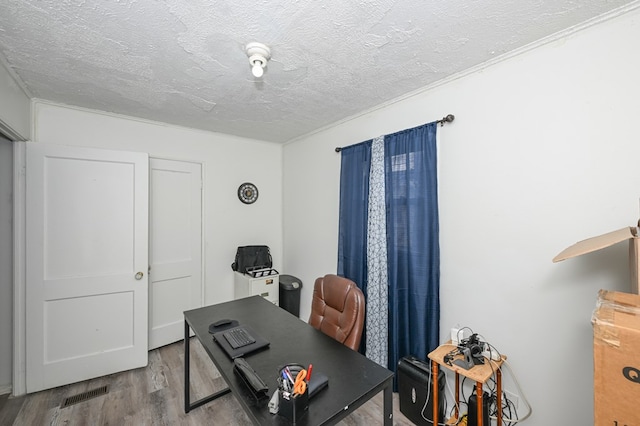 home office with a textured ceiling, visible vents, and wood finished floors