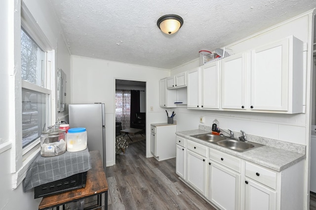 kitchen featuring dark wood-style flooring, freestanding refrigerator, white cabinetry, a sink, and a textured ceiling