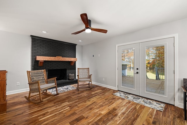 sitting room with a brick fireplace, ceiling fan, wood-type flooring, and french doors