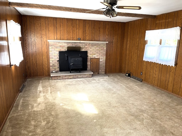 unfurnished living room with beam ceiling, wood walls, a wood stove, and ceiling fan