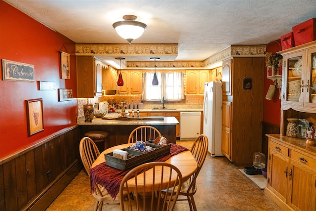 dining area featuring light floors, wooden walls, a textured ceiling, and wainscoting