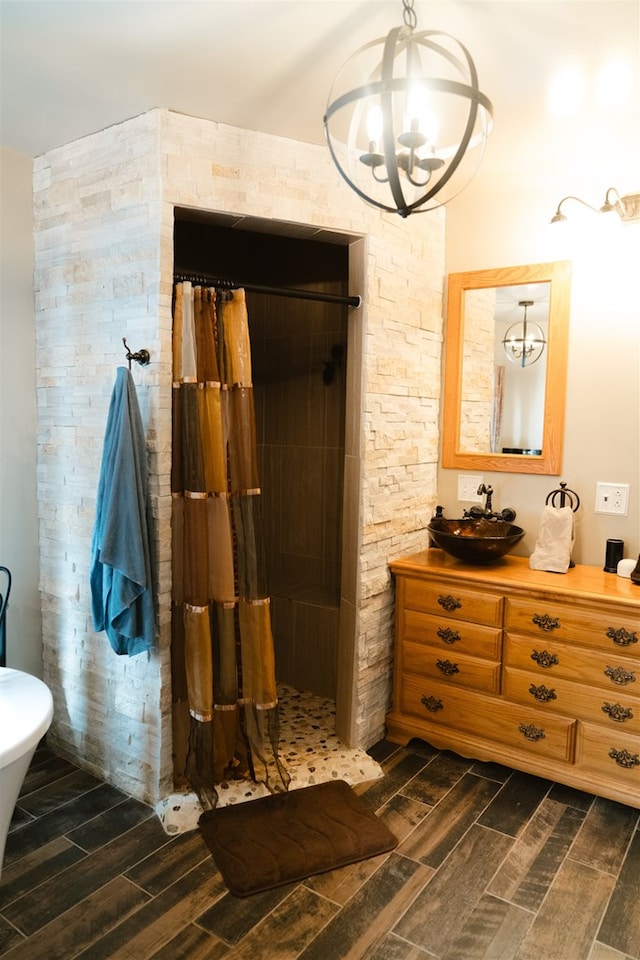 full bathroom with tiled shower, wood finish floors, vanity, and an inviting chandelier